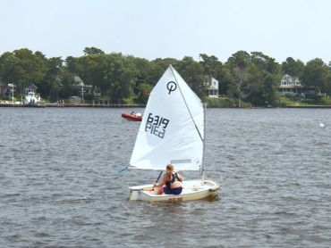 A child sailing a small boat on a lake near houses.