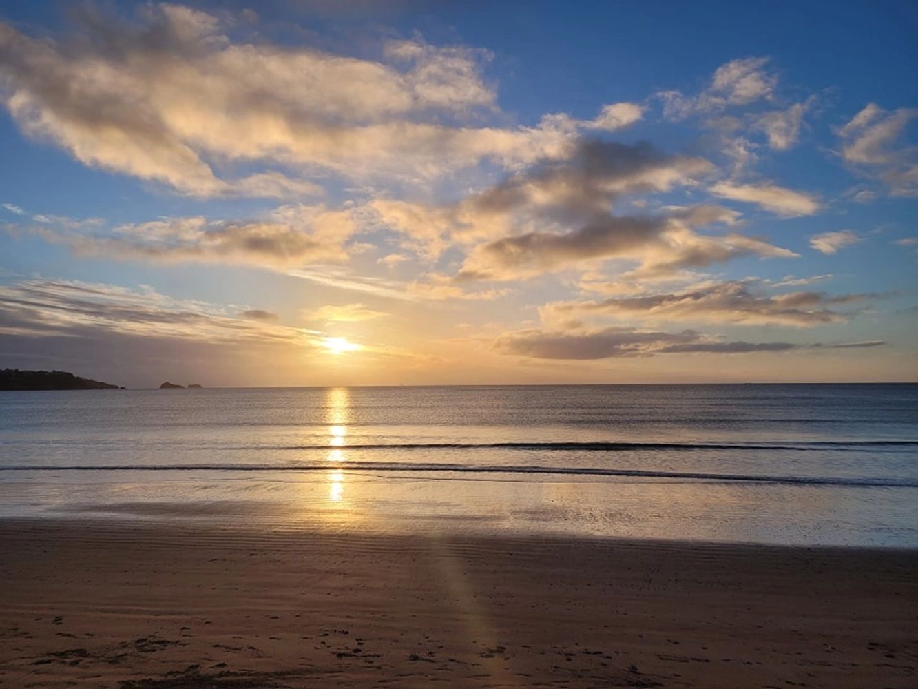 Calm beach sunset with soft clouds and gentle waves reflecting golden light.