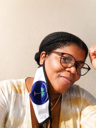 Woman with glasses and a mask hanging from one ear, smiling.