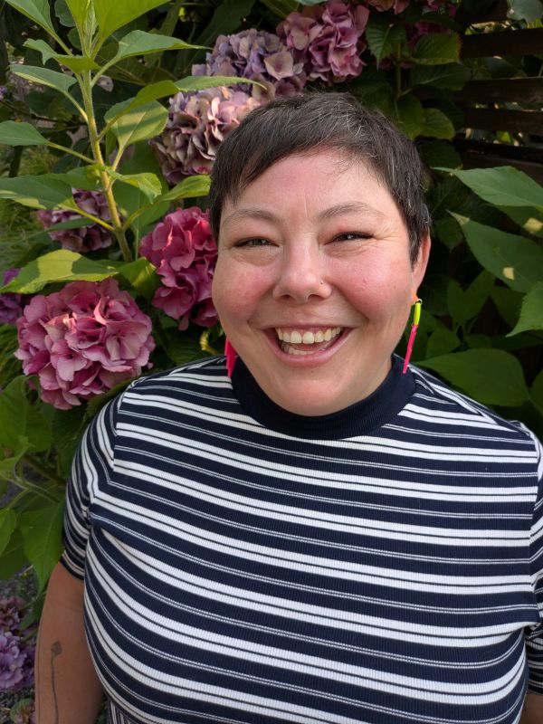 Smiling person with short hair and striped shirt in front of flowers.