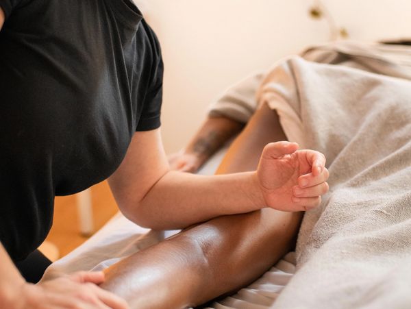 A massage therapist using their forearm to massage someone's thigh.