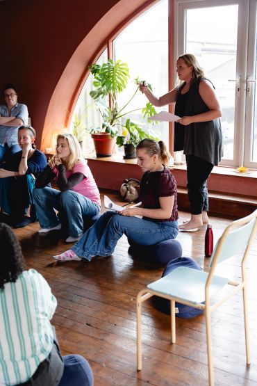 Group engaged in a discussion in a cozy room with plants and large windows.