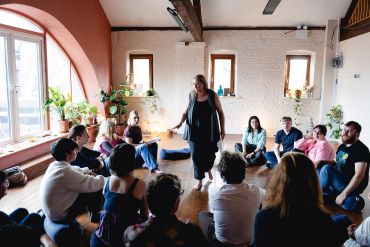 Group therapy session with participants sitting in a circle and a facilitator standing.