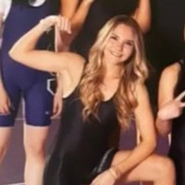Smiling young woman in black sportswear flexing her arm.