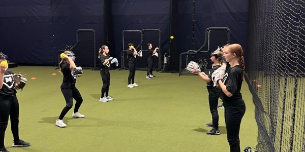 Group of kids practicing softball indoors.