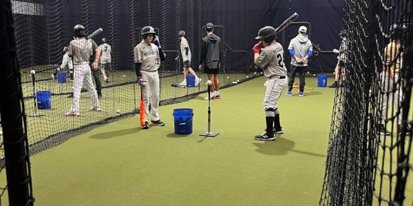 Baseball players practicing batting in an indoor cage.