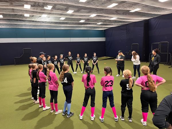 Kids in pink and black sports uniforms stand in a circle during practice.