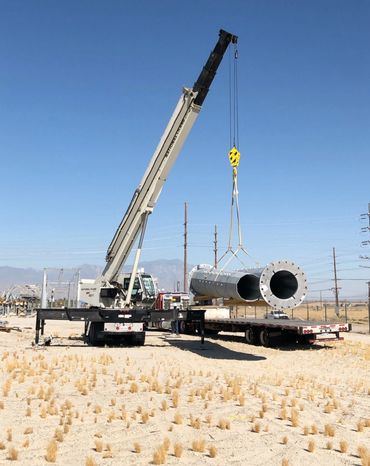 45 ton truck crane unloading steel utility pole sections.