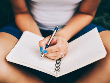 Person in white tshirt &  jean shorts sits cross-legged, ready o write in the journal in their lap.