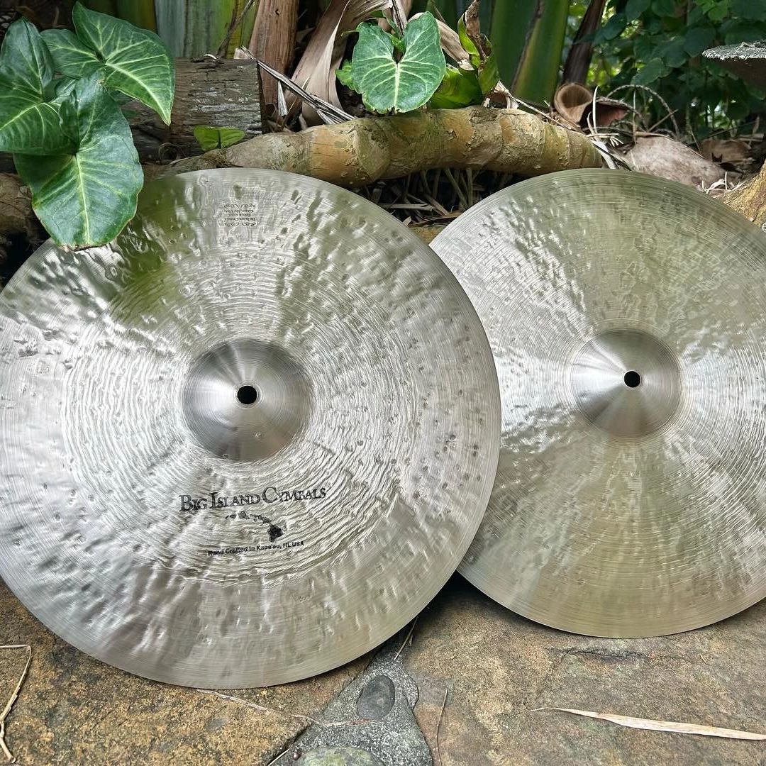 Two shiny Big Island Cymbals placed outdoors on a stone surface.