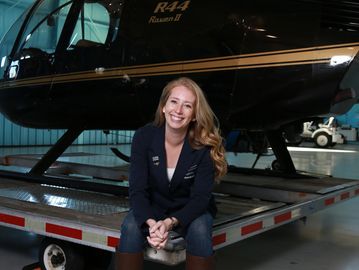 Heather Howley sitting in front of R44 helicopter