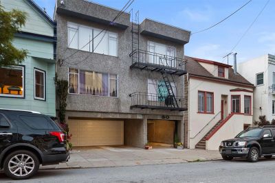 Gray multi-story house with fire escapes and two parked cars.