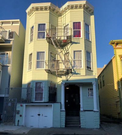 Three-story green and yellow building with fire escape under clear blue sky.