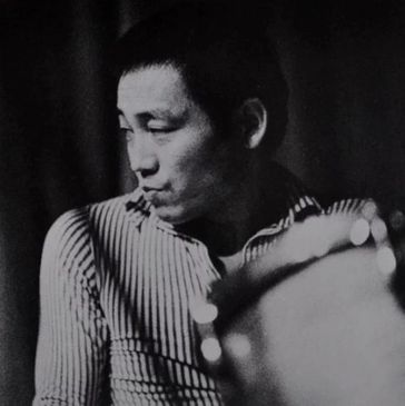 Black and white portrait of a man in a striped shirt, looking to the side.