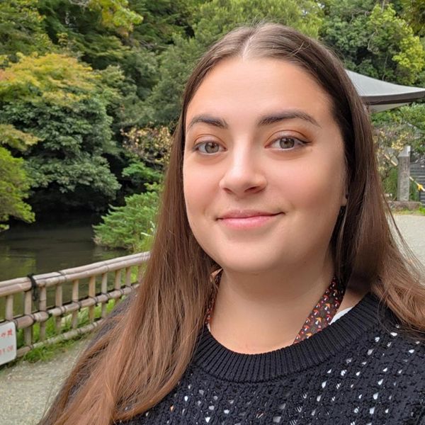 Young woman smiling outdoors near greenery.