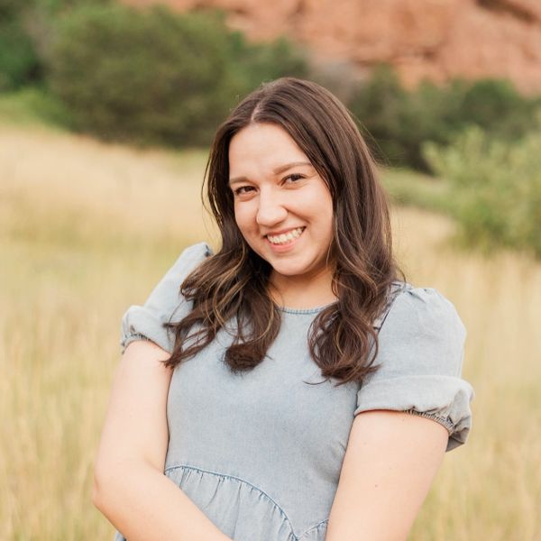 A young woman smiling outdoors in a natural grassy area.