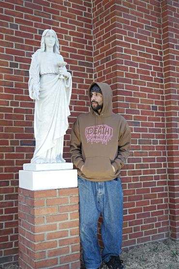 Man in a brown hoodie standing next to a white statue.