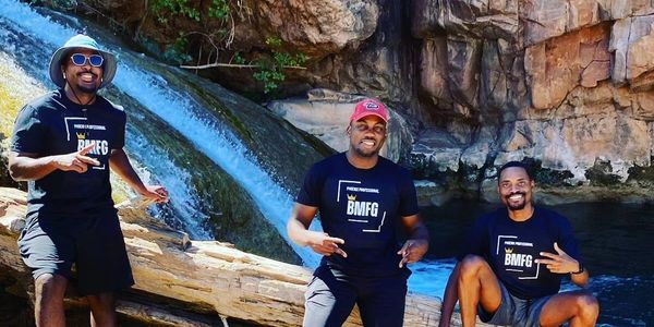 Three men posing happily by a waterfall in matching BMFG shirts.