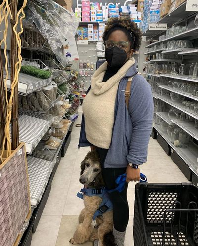 a black femme presenting person and their service dog standing in an aisle of a craft store