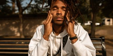 African-American male seated outside on a bench in summer with both hands on his face, eyes closed