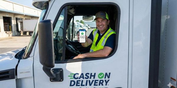 Smiling delivery driver shows phone with payment app in truck cab.