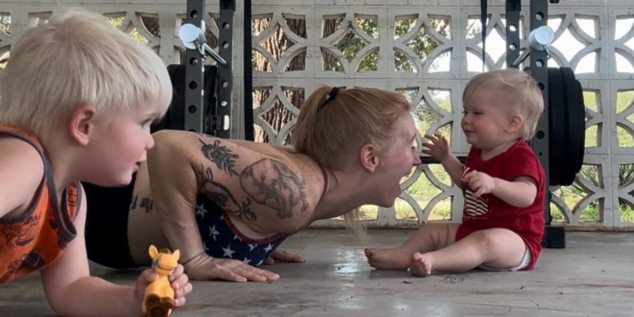 Woman doing push-ups interacting with two young children.