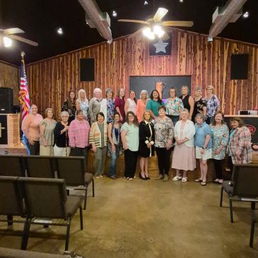 Group of women posing inside a wooden-paneled room with an American flag.