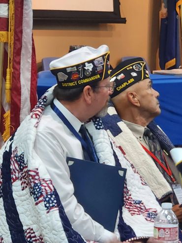 Two veterans wrapped in patriotic quilts at a formal event.