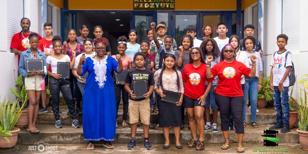 Group photo of diverse students and teachers outside a building, holding tablets.