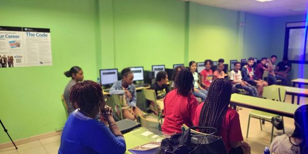 A group of people sitting in a classroom or meeting room with green walls.