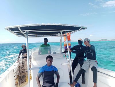 Five men on a boat in wetsuits against a blue sea and sky.