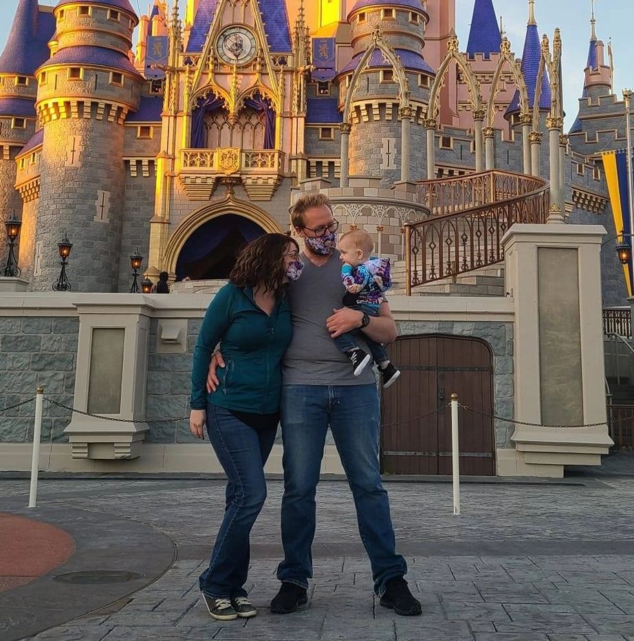 Family of three in front of a castle, wearing masks.