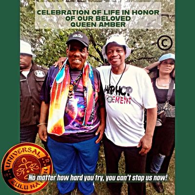 Two men smiling at a celebration honoring Queen Amber in a park.