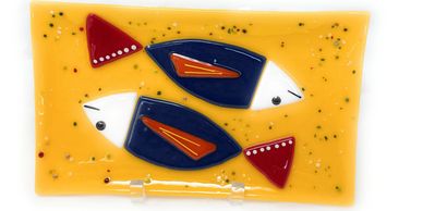 Two navy blue fish with red tails on a marigold colored fused glass plate.