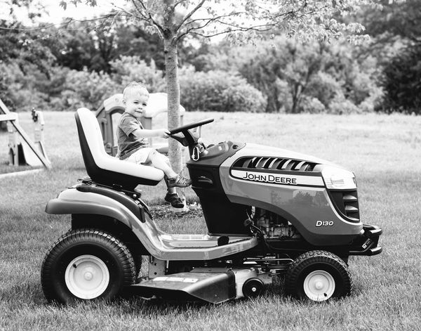 A child sitting on a John Deere riding lawn mower outdoors.