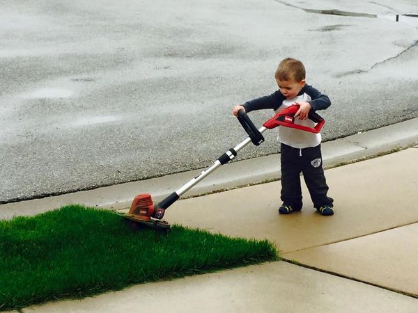 A young child using a grass trimmer on a sidewalk edge.