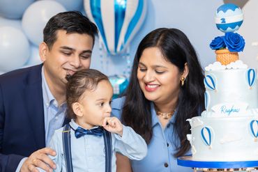 A family celebrating a toddler's 2nd birthday with a themed cake and balloons.