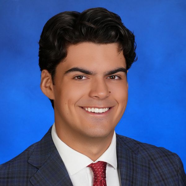 Smiling young man in business attire against a blue background.