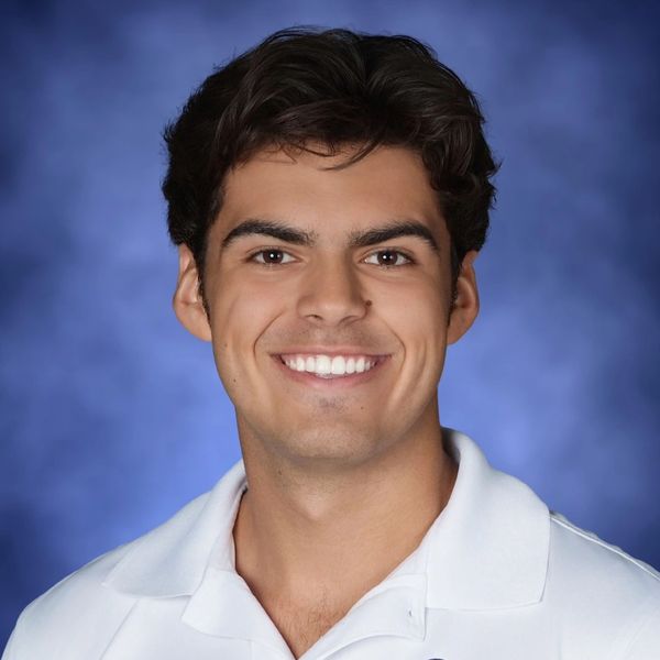Young man smiling in a white polo shirt against a blue background.