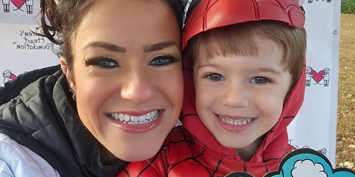 A smiling woman and child dressed as Spider-Man pose for a close-up photo.