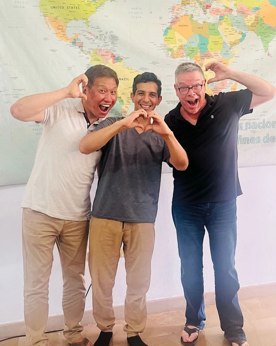 Three men making heart shapes with their hands and smiling.