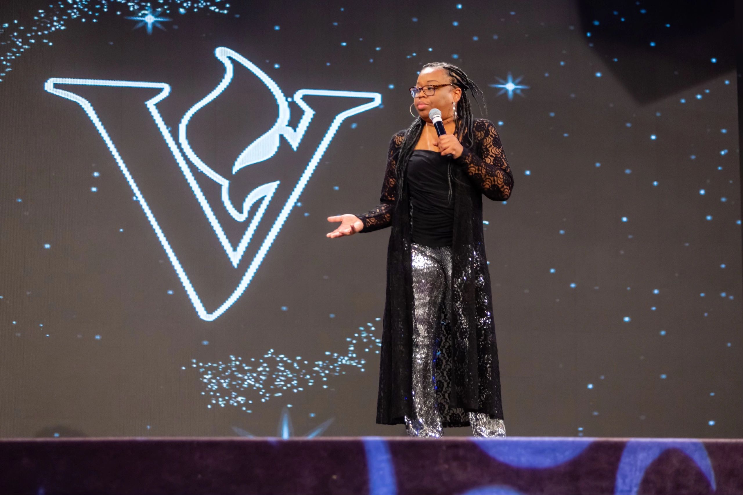 Speaker on stage with a microphone and starry background.