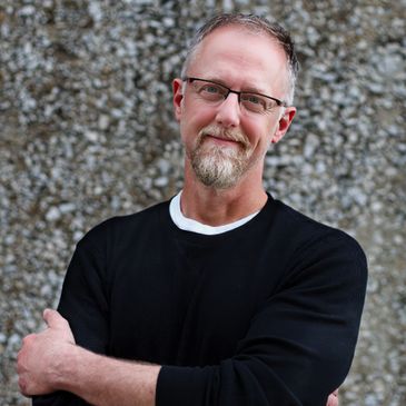Middle-aged man with glasses and beard smiling, wearing a black sweatshirt.