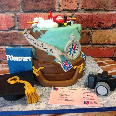 Travel-themed cake with airplane, passport, and camera decorations.