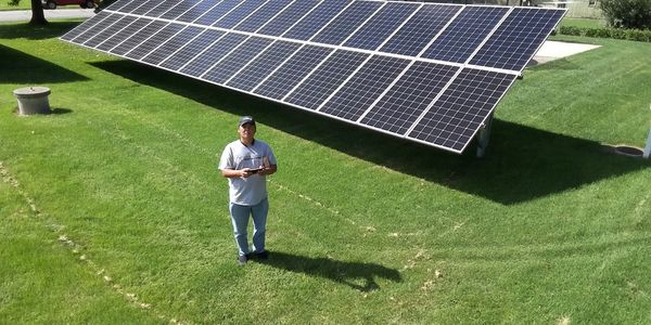 Man stands on grass near ground-mounted solar panels on a sunny day.