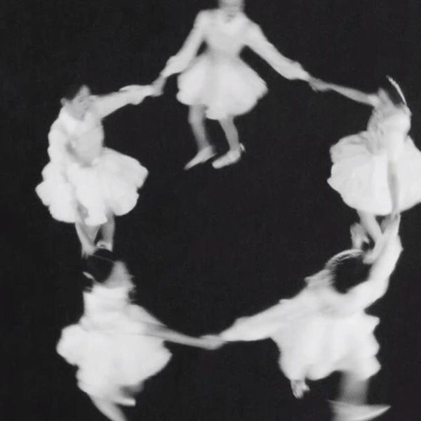 Blurry black-and-white image of five girls in dresses holding hands in a circle.