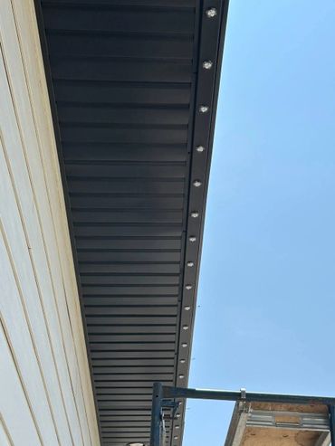 Black soffit with recessed lights under a roof against a clear blue sky.