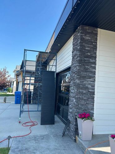 Scaffolding set up outside a modern house with stone and siding exterior on a clear day.