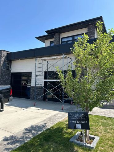 Modern house under construction with scaffolding and a company sign on the lawn.