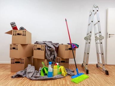 Cleaning supplies and packed boxes next to a ladder in a room.